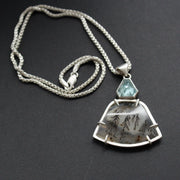 striking pendant by jewellery designer Carin Lindberg featuring small pale blue stone above a grey and detailed agate stone in a silver setting on a silver chain