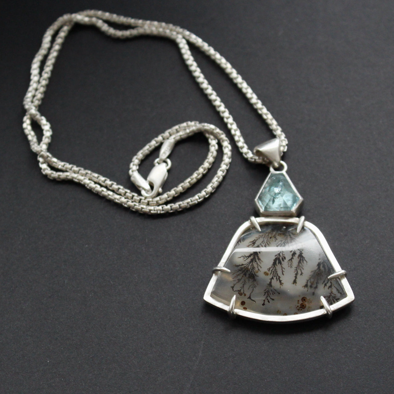 striking pendant by jewellery designer Carin Lindberg featuring small pale blue stone above a grey and detailed agate stone in a silver setting on a silver chain