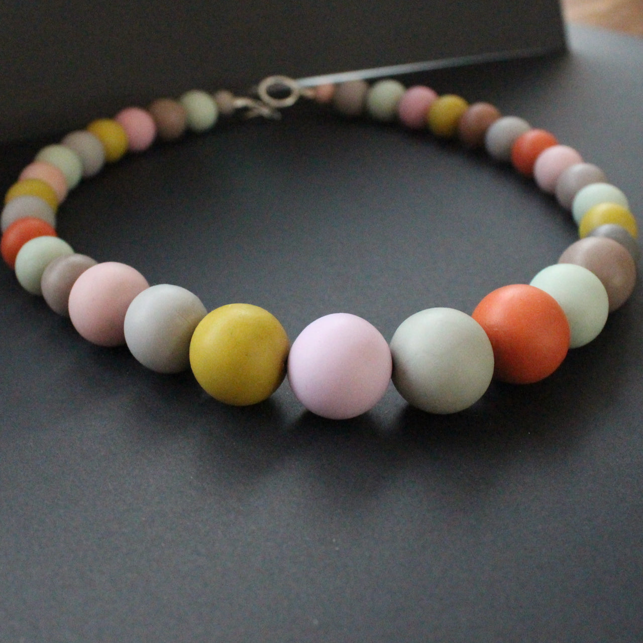Graduated size round beaded necklace in muted earth tones by artist Clare Lloyd.