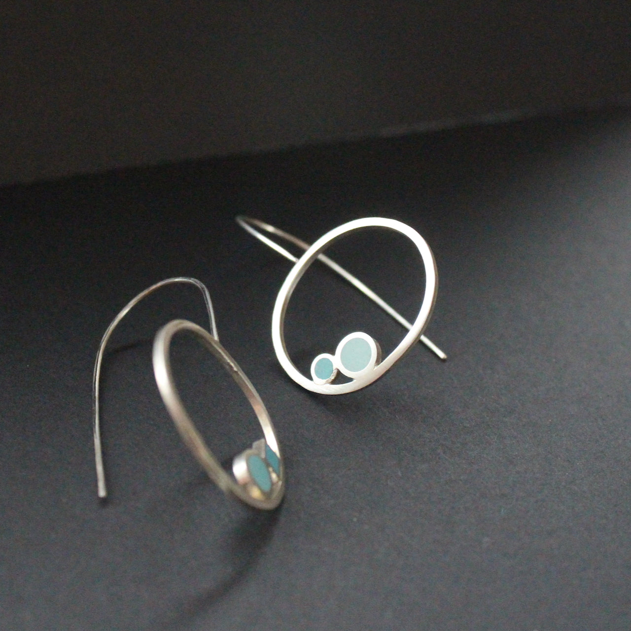 Round drop earrings with 2 dots of turquoise and aqua sitting inside the rings by artist Clare Lloyd.