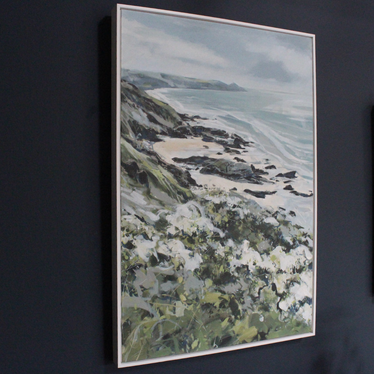 a framed painting of cliffs falling away from coastline with sandy beach and blue sea to left, Rame Head peninsula in the background by Cornish artist Imogen Bone