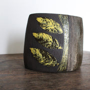 A ceramic vessel with yellow leaf shaped glaze on dark brown clay by Cornish Artist Anthea Bowen