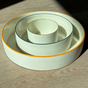 By the Line Pottery, set of three nesting bowls made of porcelain with a coloured rim, the largest has an orange rim, then dark green, then olive