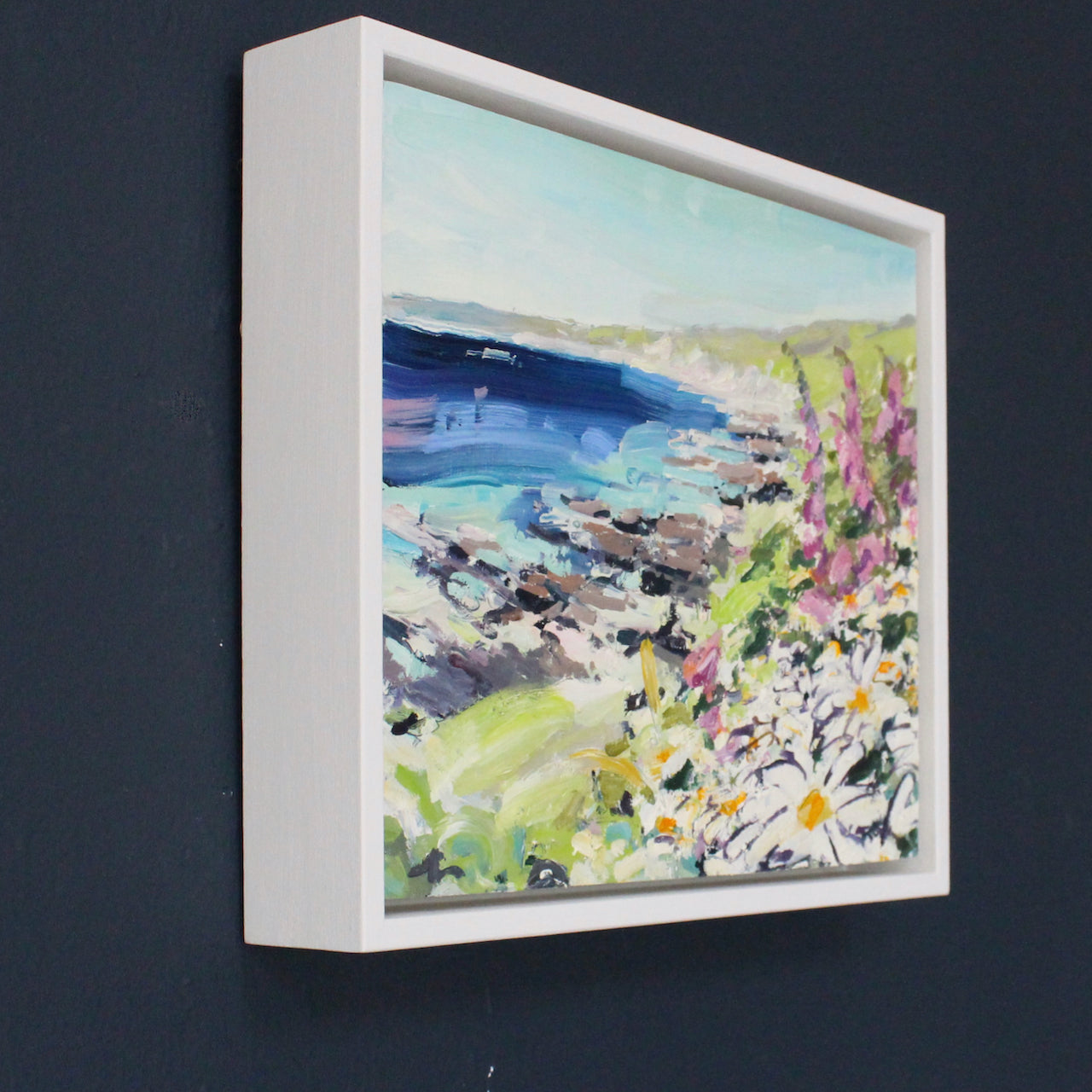 Painting of White and purple flowers in the foreground on headland with blue sea and grey rock formations by artist Jill Hudson