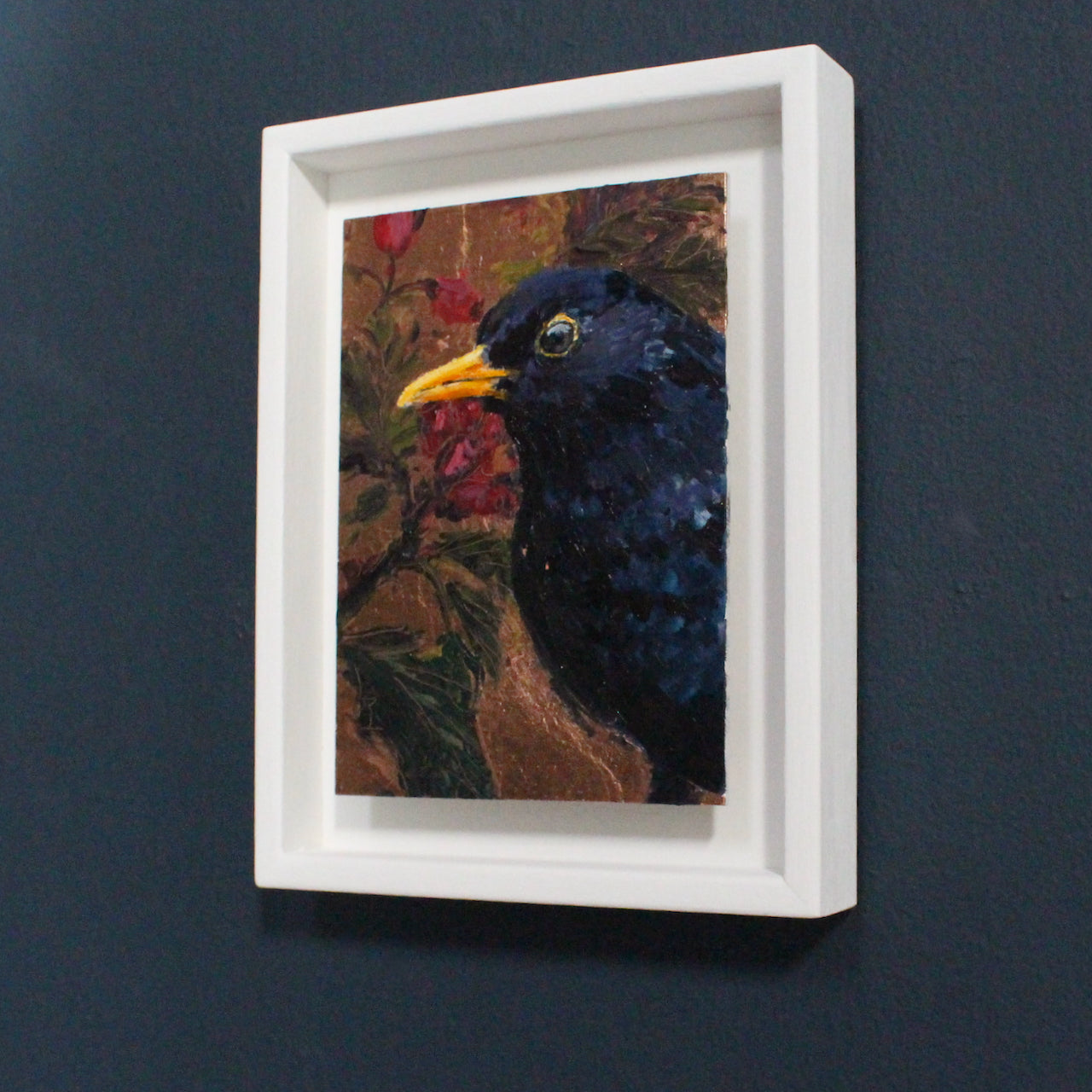 a framed painting by Jill Hudson of a blackbird on background of gold with red berries and  green leaves,
