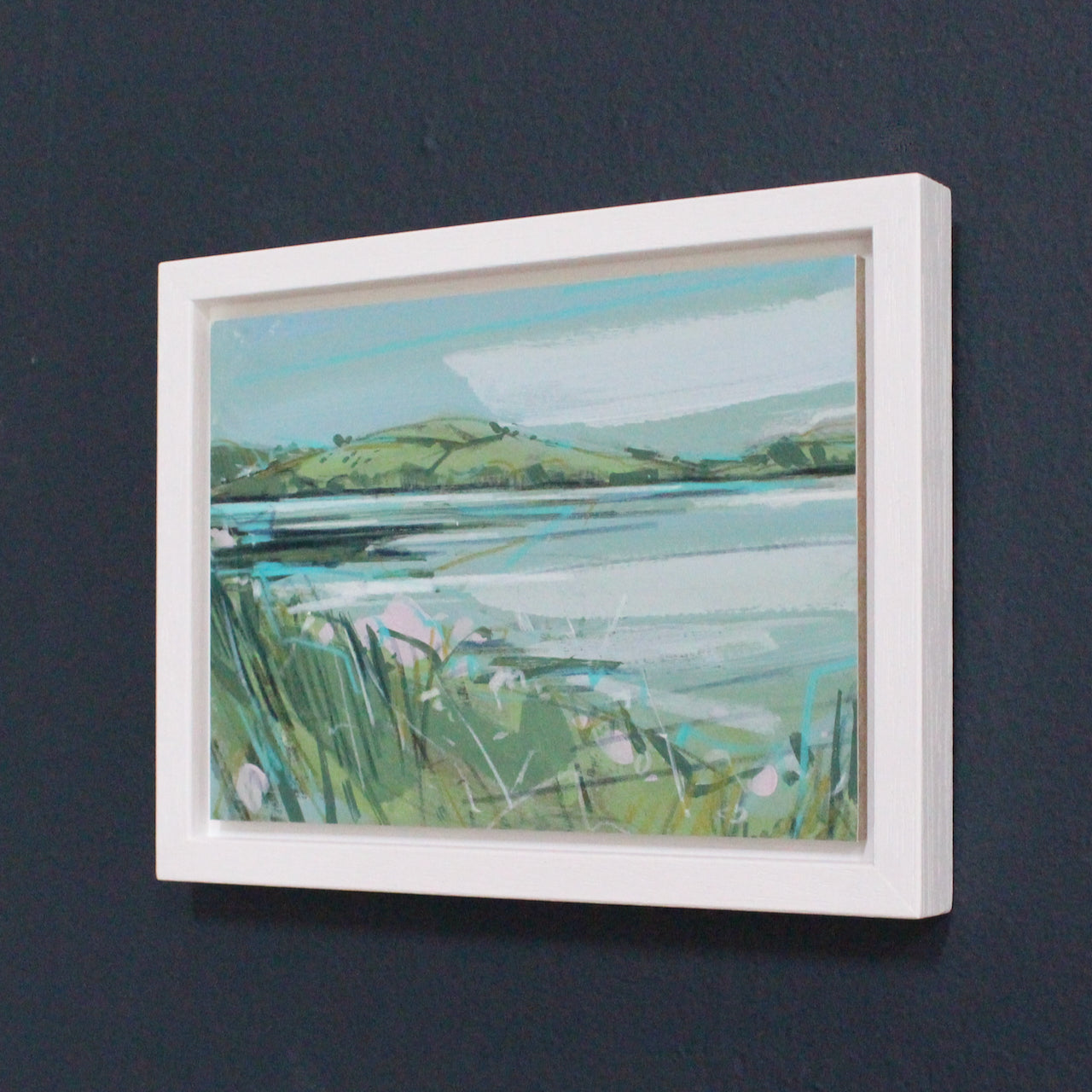 a framed Imogen Bone small landscape of river Lynher in Cornwall with green hills, pale blue river and pink flowers on the riverbank.