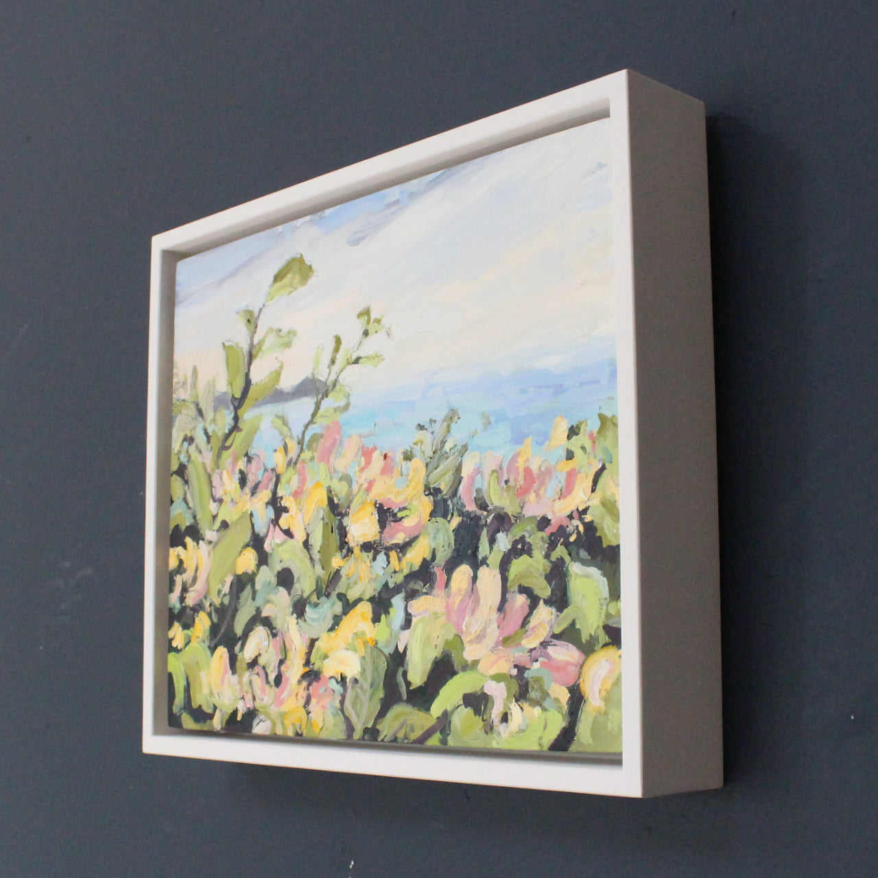 a framed Jill Hudson painting of flowers and foliage of pinks, greens and yellows in foreground, sea and Rame Head peninsula  in the background