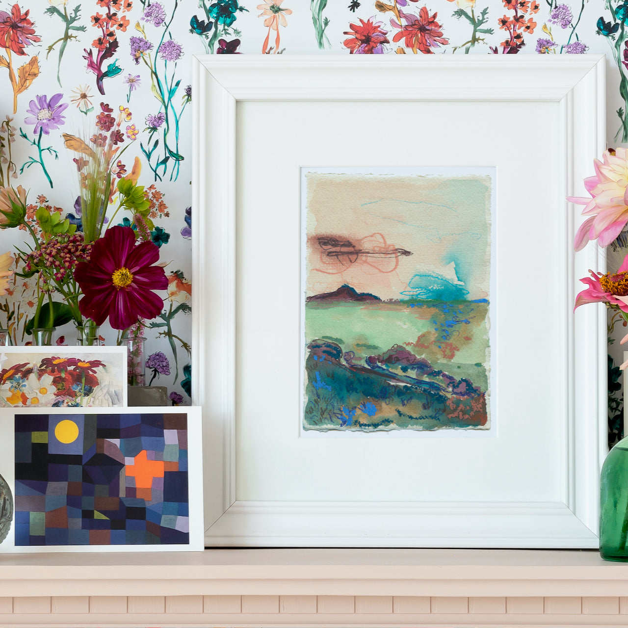framed painting by artist Lucy Innes Williams seascape in  tones of blue and pinks  it is framed and propped against a floral wallpaper 