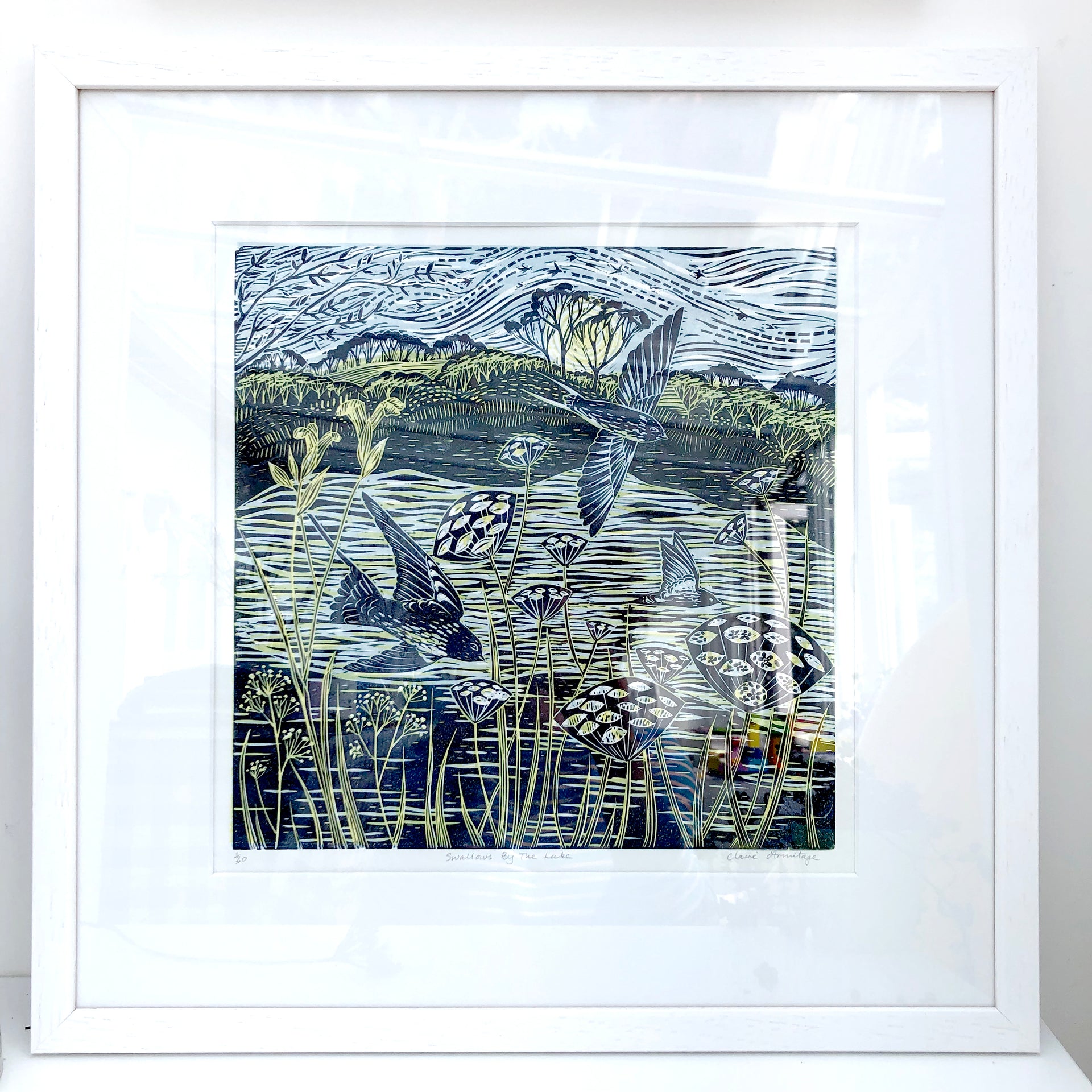 Lino print by artist Claire Armitage of swallows over lake in blue and yellow tones