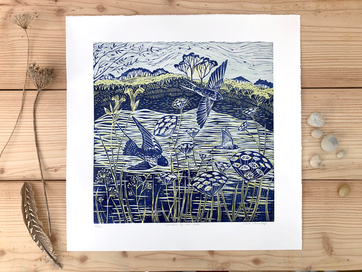 Lino print by artist Claire Armitage of swallows over lake in blue and yellow tones.