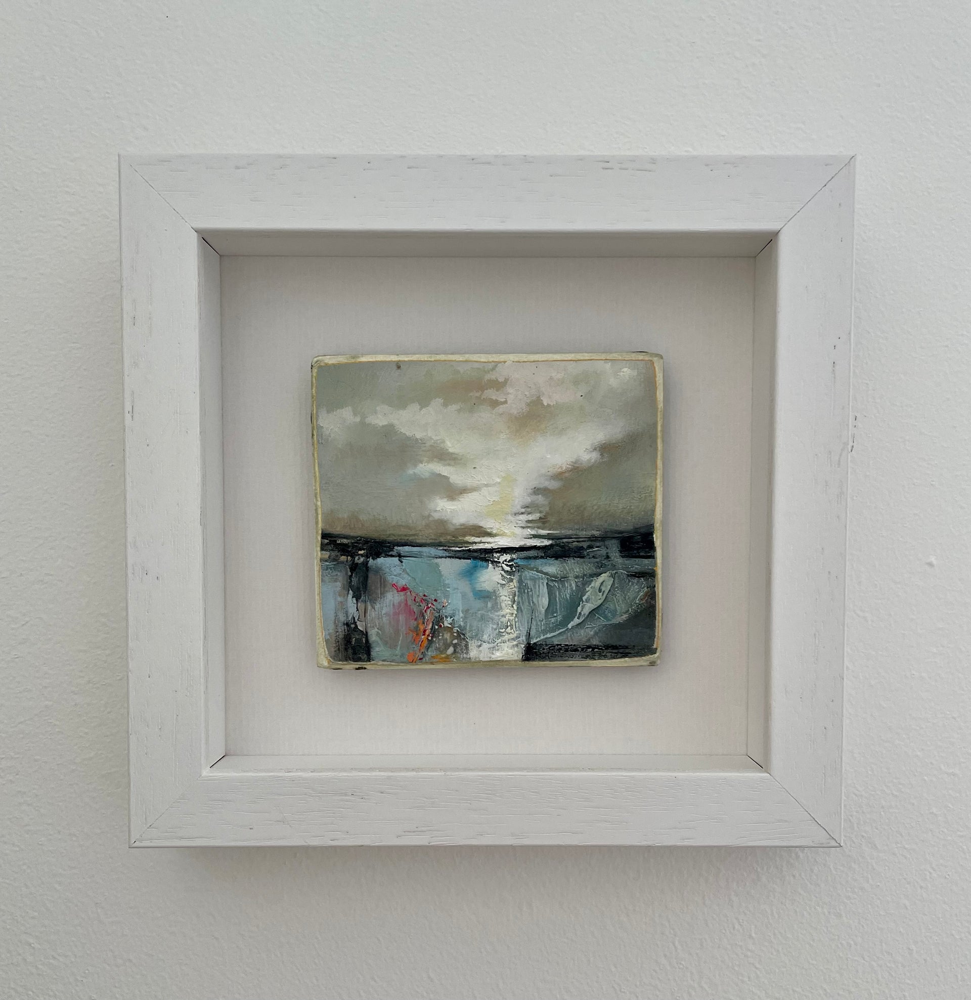a small framed painting by artist Julie Ellis of a dark brooding sky over a blue, black and pink sea