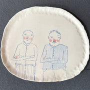 Becca Brown ceramic plate decorated with drawing of two men with their arms crossed
