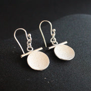 Beverly Bartlett silver drop earrings with a textured silver disc under a silver horizontal bar and silver chain.