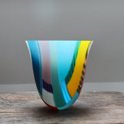 tall and gently curved multi-coloured glass vase on a wooden table it is made by Ruth Shelley