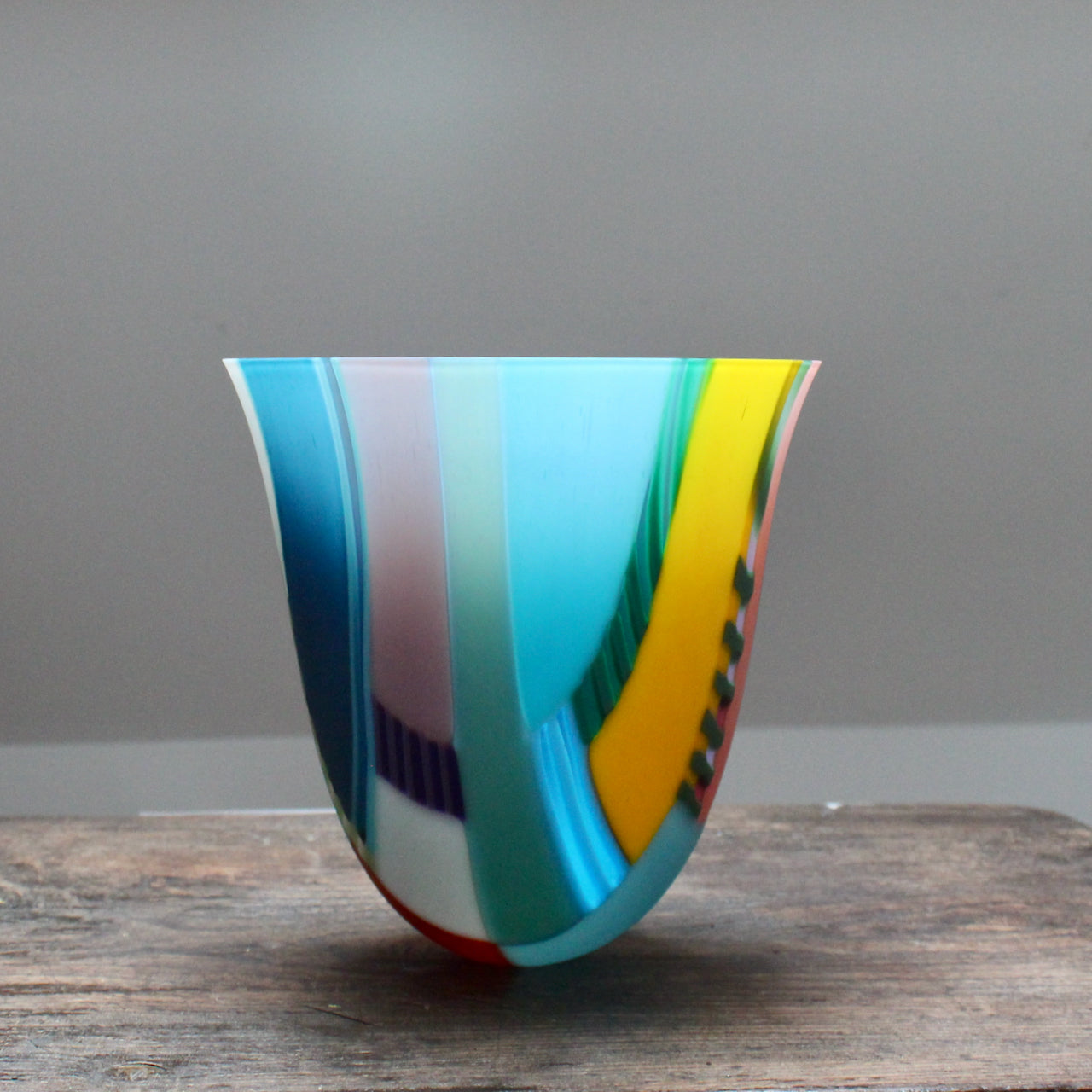 tall and gently curved multi-coloured glass vase on a wooden table it is made by Ruth Shelley