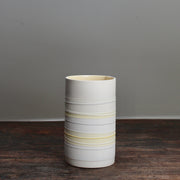 white ceramic cylinder vase with pale yellow stripes on a wooden table