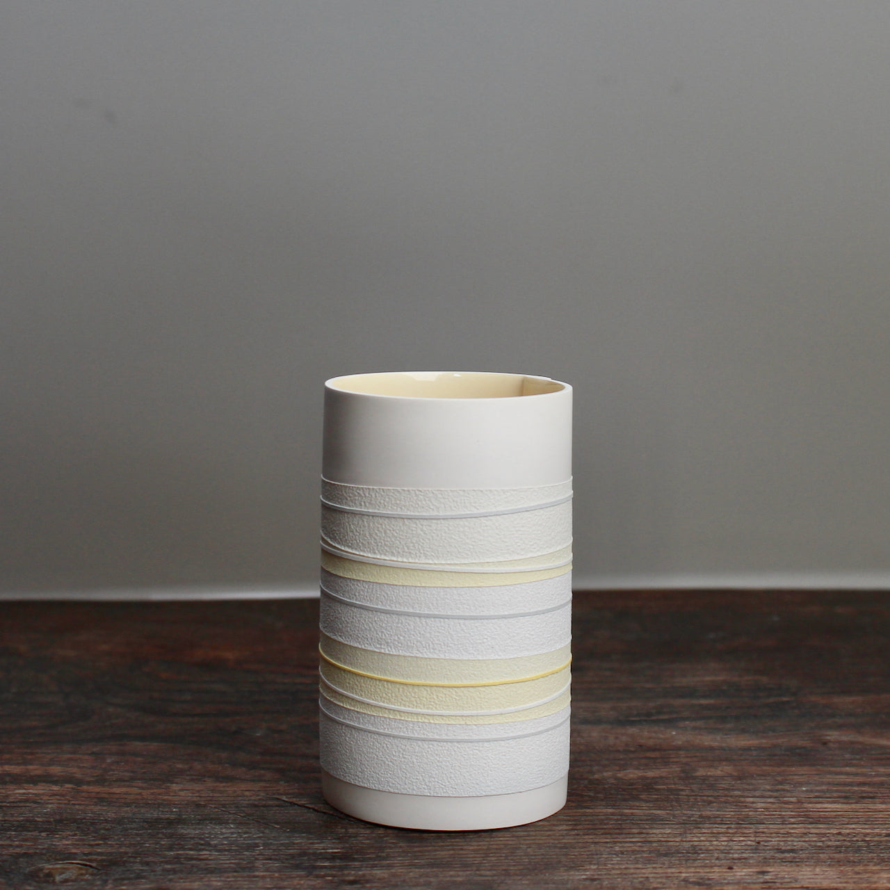 white ceramic cylinder vase with pale yellow stripes on a wooden table