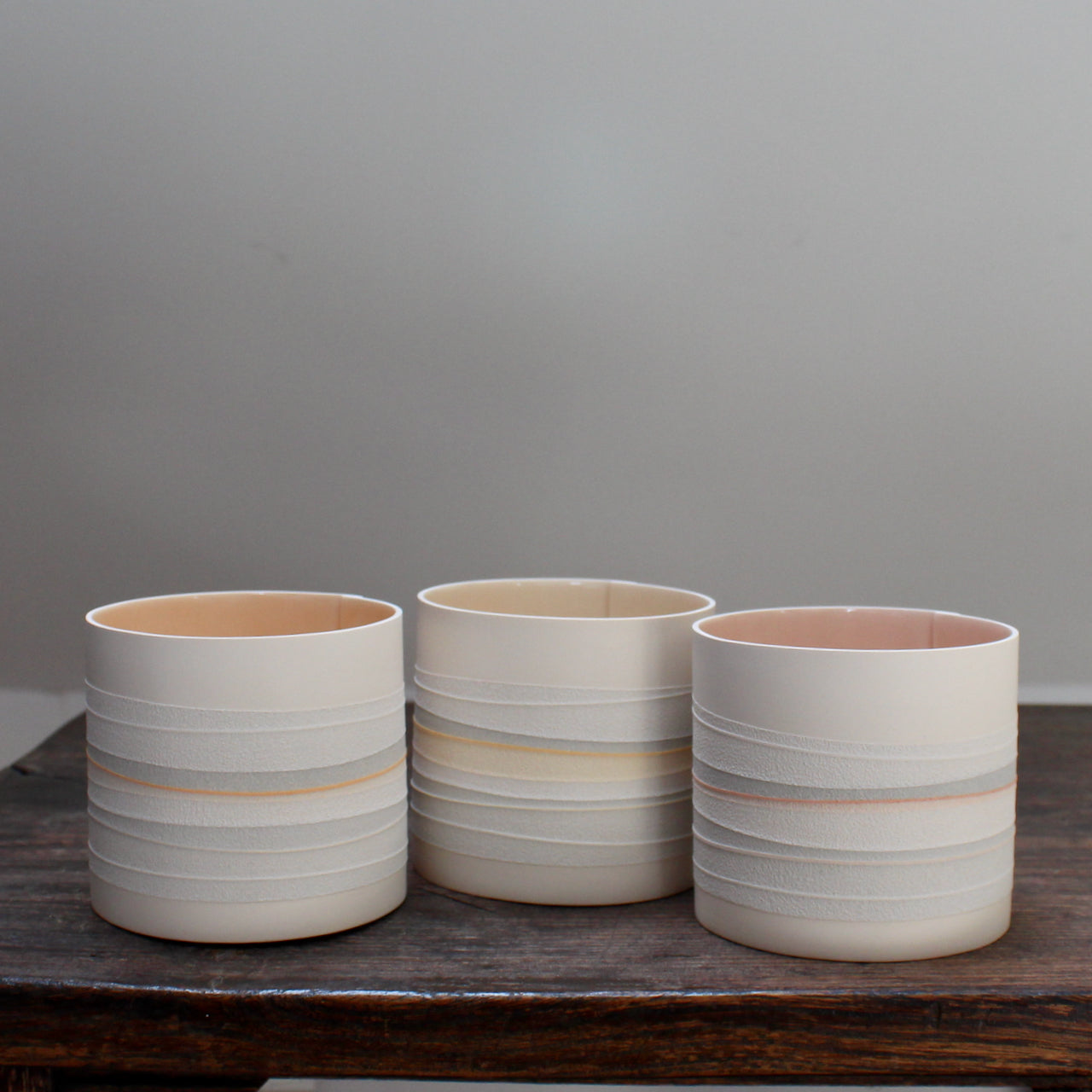 three ceramic pots with pale pink interiors and pastel stripes on the outside 