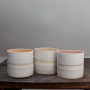 a set of three small ceramic pots with pale interiors and pastel stripes on the outside.
