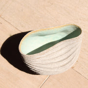 a stoneware bowl which has been hand carved to create a slumped and ribbed effect on the exterior with a pale green glaze inside it was made by British ceramic artist Michele Bianco