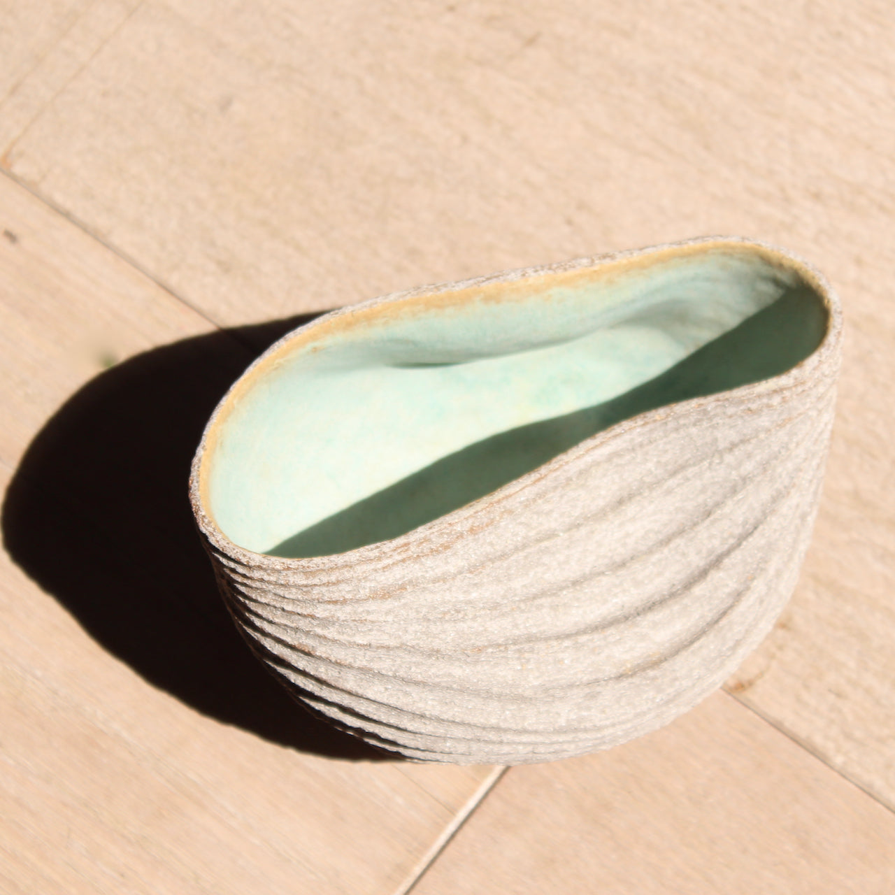 a stoneware bowl which has been hand carved to create a slumped and ribbed effect on the exterior with a pale green glaze inside it was made by British ceramic artist Michele Bianco