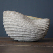 stoneware bowl which has been hand carved to create a slumped and ribbed effect on the exterior with a pale green glaze inside it was made by ceramicist Michele Bianco