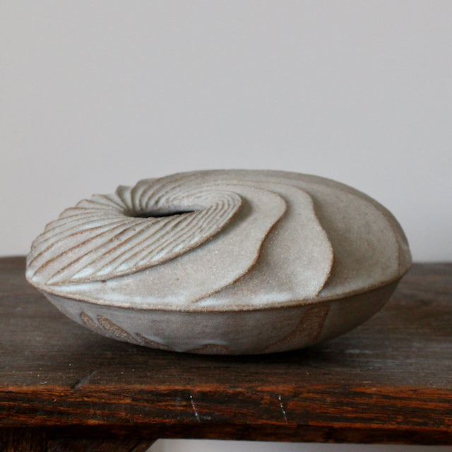 A round and carved ceramic vessel by Michele Bianco photographed on a dark wood table