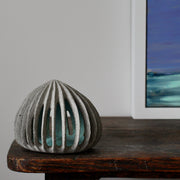 pale green carved and semi open stoneware ceramic pod shaped sculpture by Michele Bianco next to the corner of a painting in a white frame. 