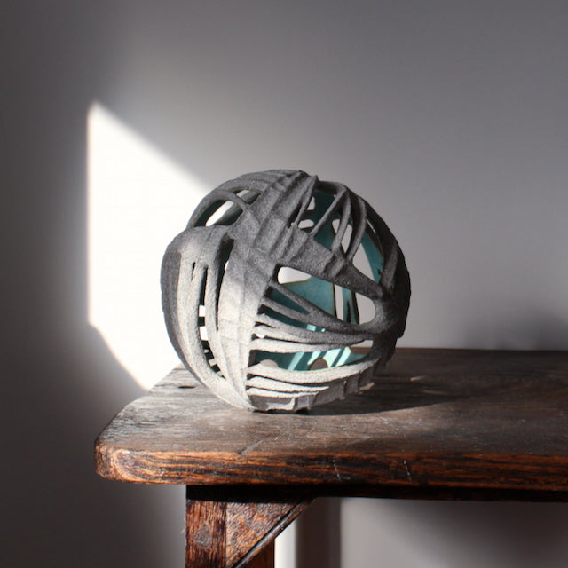 Michele Bianco carved and open round ceramic sculpture photographed on a wooden table with a beam of sunlight. 