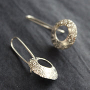 a pair of silver drop earrings with a hollow centre and a delicate pattern of circles by Ann Bruford