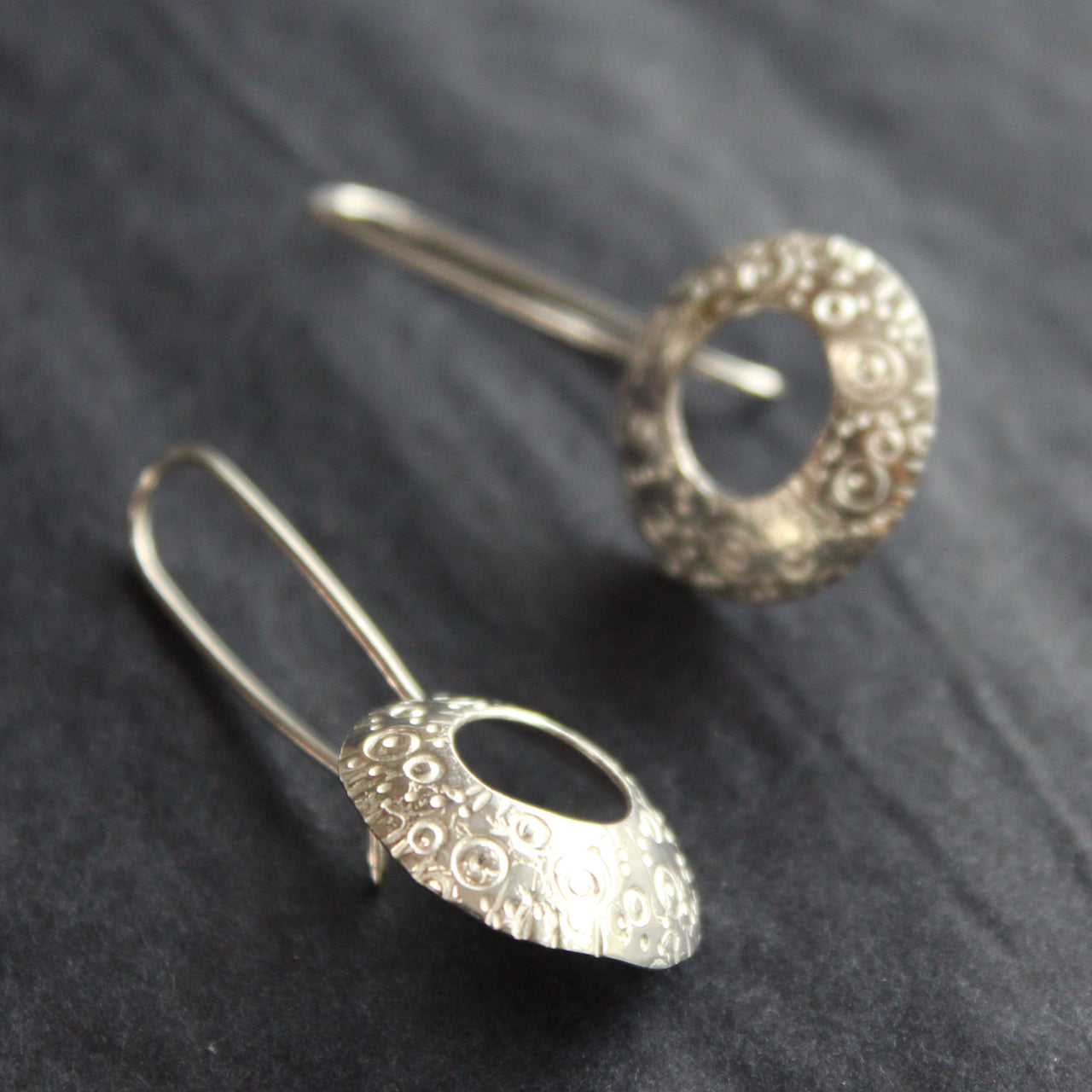a pair of silver drop earrings with a hollow centre and a delicate pattern of circles by Ann Bruford