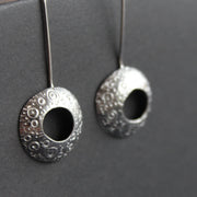 a pair of silver drop earrings with a hollow centre and a delicate pattern of circles by UK jeweller Ann Bruford