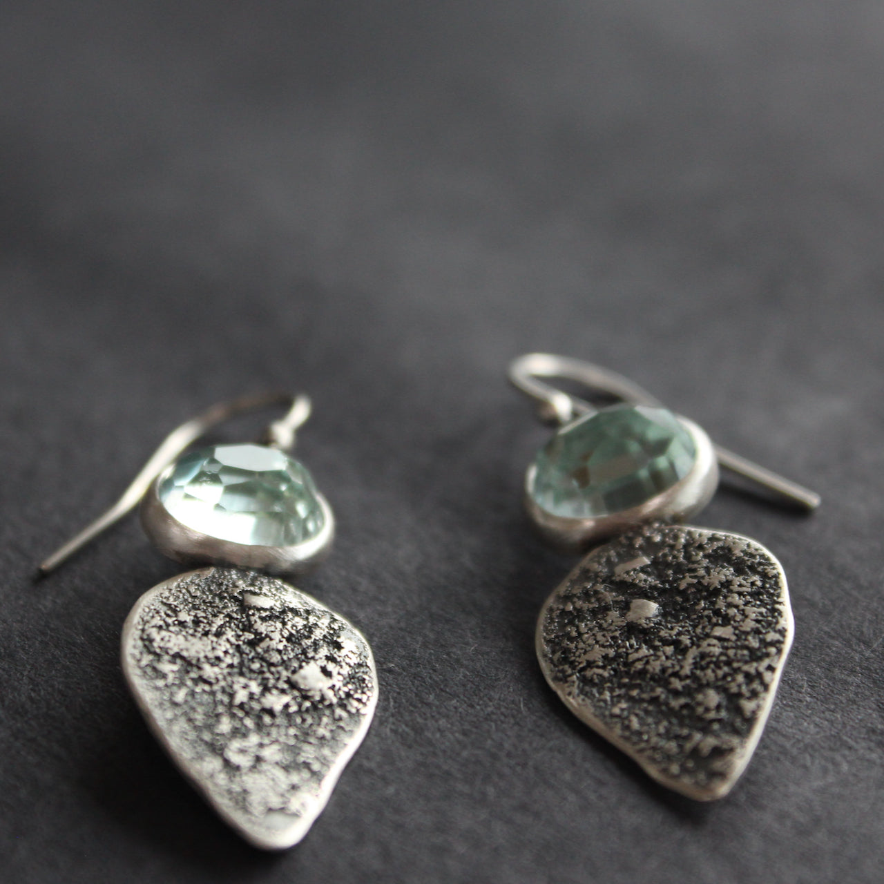 Textured silver with aquamarine stone drop earrings on a dark grey background