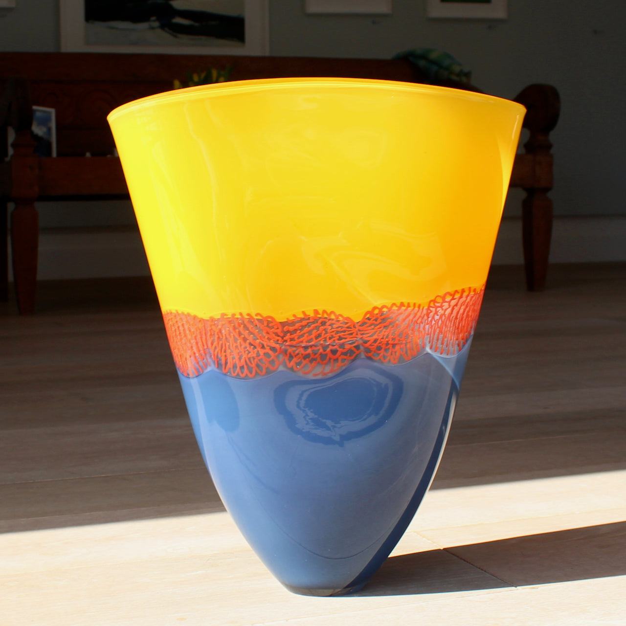 a glass vessel by Benjamin Lintell with a blue base and orange top divided by a red detail photographed in the sunshine