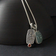 double silver pendant on a silver chain with one green stone and one small orange topaz it is by jeweller Carin Lindberg