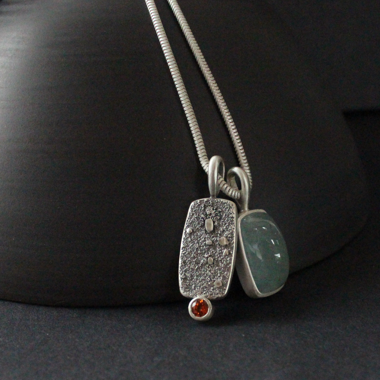 double silver pendant on a silver chain with one green stone and one small orange topaz it is by jeweller Carin Lindberg