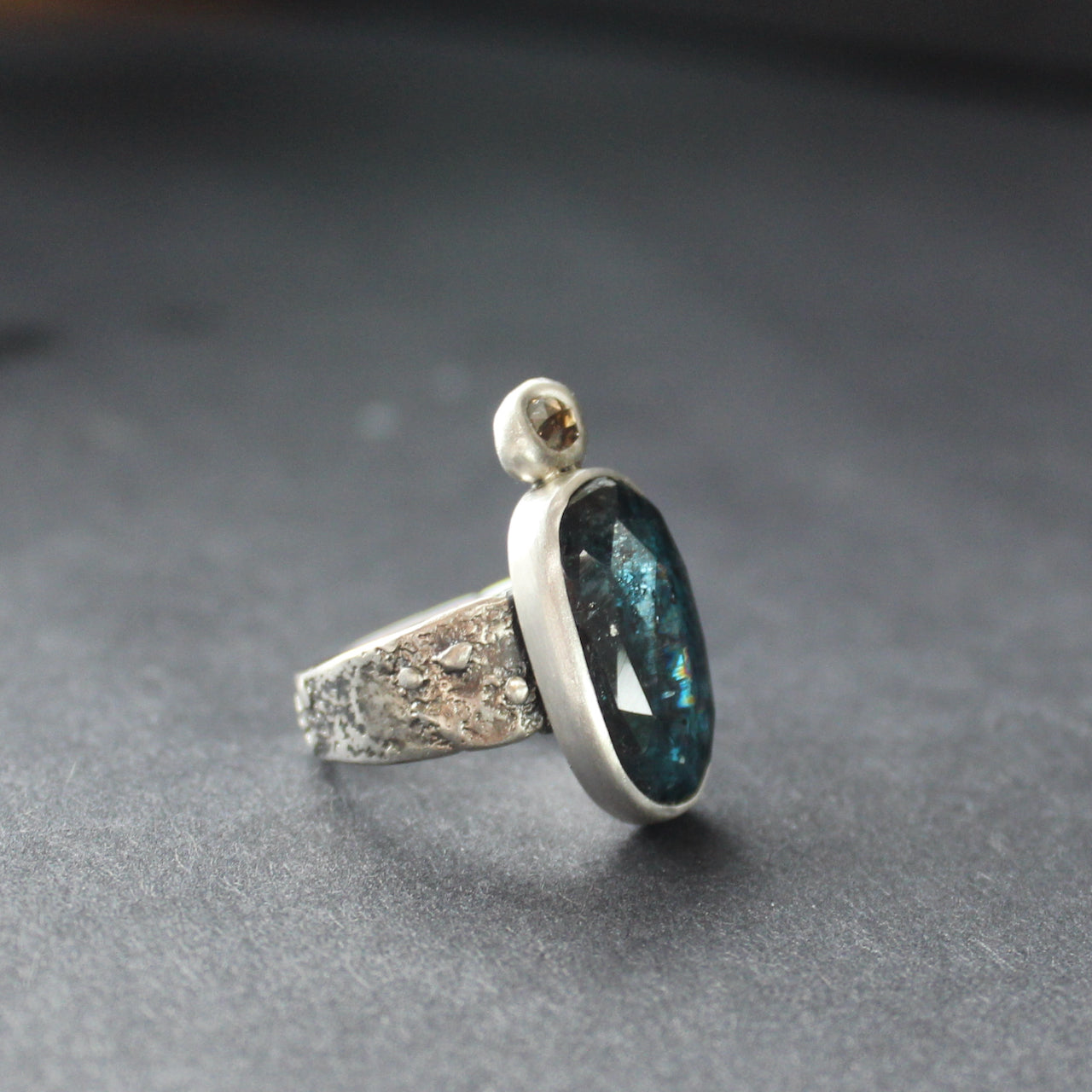 textured silver  ring with a large dark blue green stone and smaller brown diamond by jeweller Carin Lindberg.