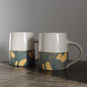 a pair of ceramic mugs with bottom half glazed in blue with abstract yellow marks by UK ceramicist Kate Welton