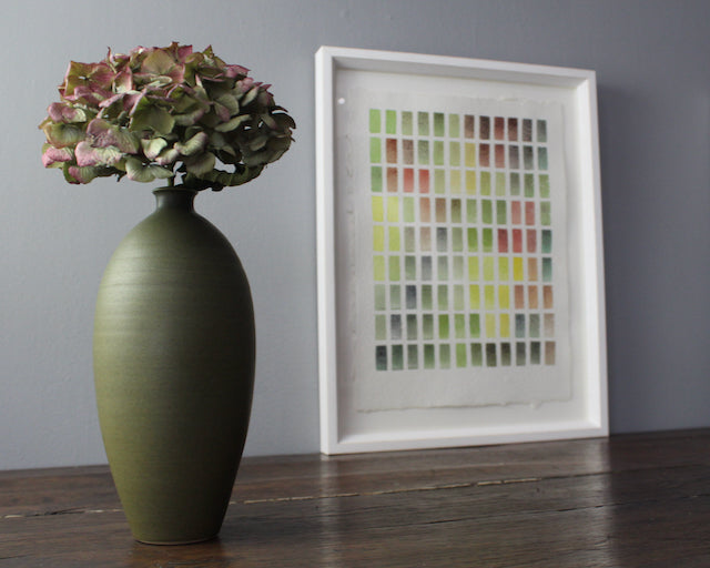 Abstract painting of yellow, pink and green rectangles bordered by white paper. Painted by David Muddyman next to green ceramic bottle with hydrangea in it.