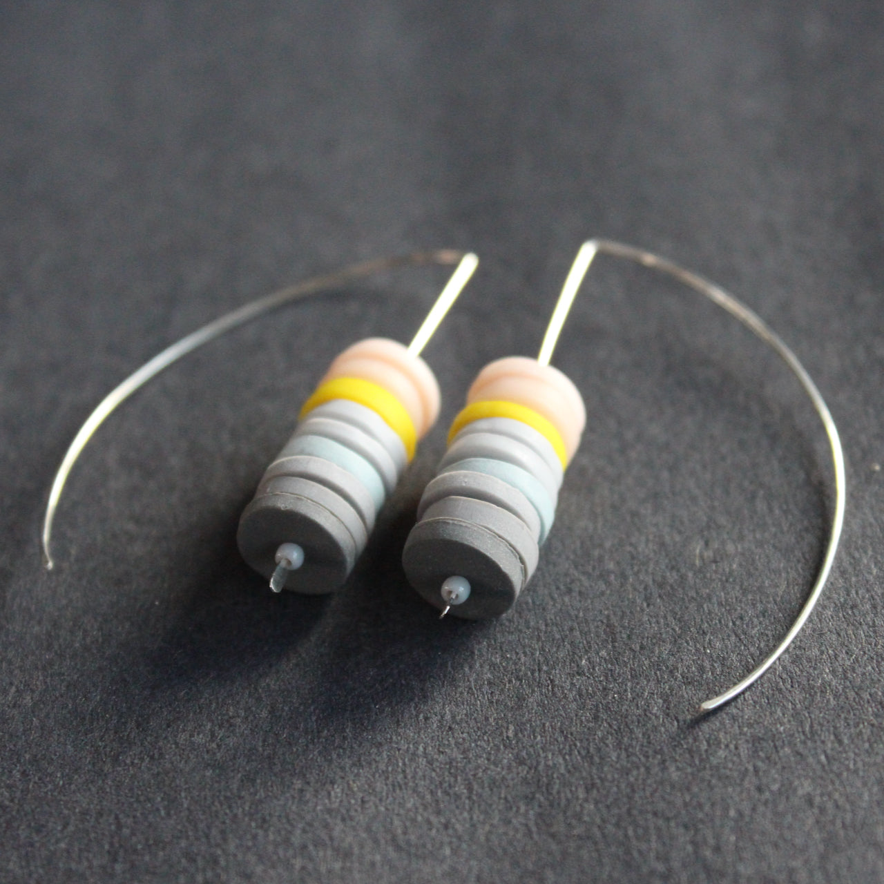 a pair of earrings made of small discs on top of each other in shades of grey and pink by jewellery designer Clare Lloyd