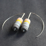 a pair of earrings made of small discs on top of each other in shades of grey and pink by jewellery designer Clare Lloyd
