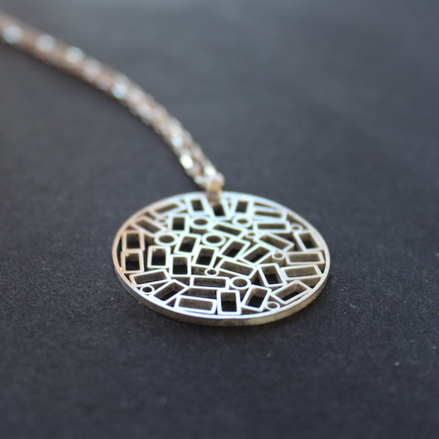 The Byre Gallery Cambium pendant by Beverly Bartlett it is A round silver pendant on a chain, the centre is made up of cut out rectangles and small circles, on a silver chain