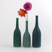 A trio of Lucy Burley ceramic bottles in shades of teal  the middle bottle has two pink flowers in it.