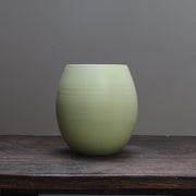 almond green curved vase by Lucy Burley on a wooden table