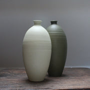 A pale green and a dark green ceramic bottle side by side on a wooden table