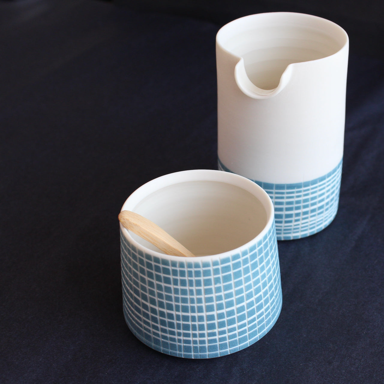 a porcelain pourer and condiment bowl set by Kathryn Sherriff of By the Line Pottery each is designed with a blue cross hatch glaze
