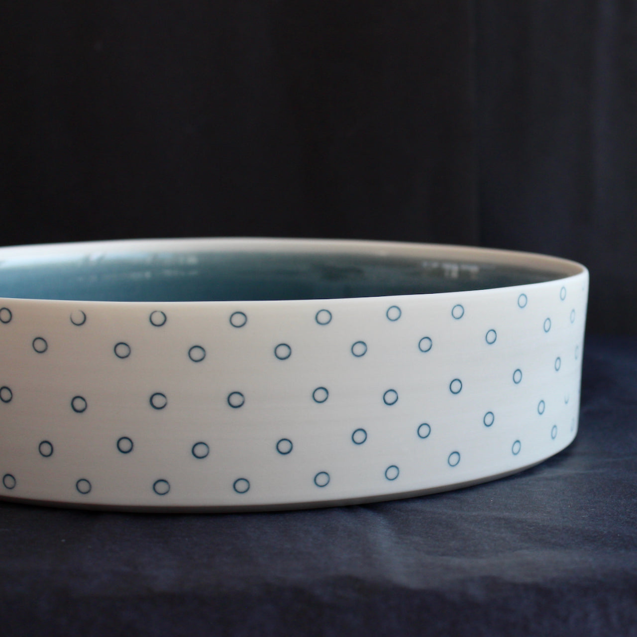 close up detail of a porcelain serving dish by Kathryn Sherriff of By the Line Pottery with a blue interior and a blue circle design on the exterior