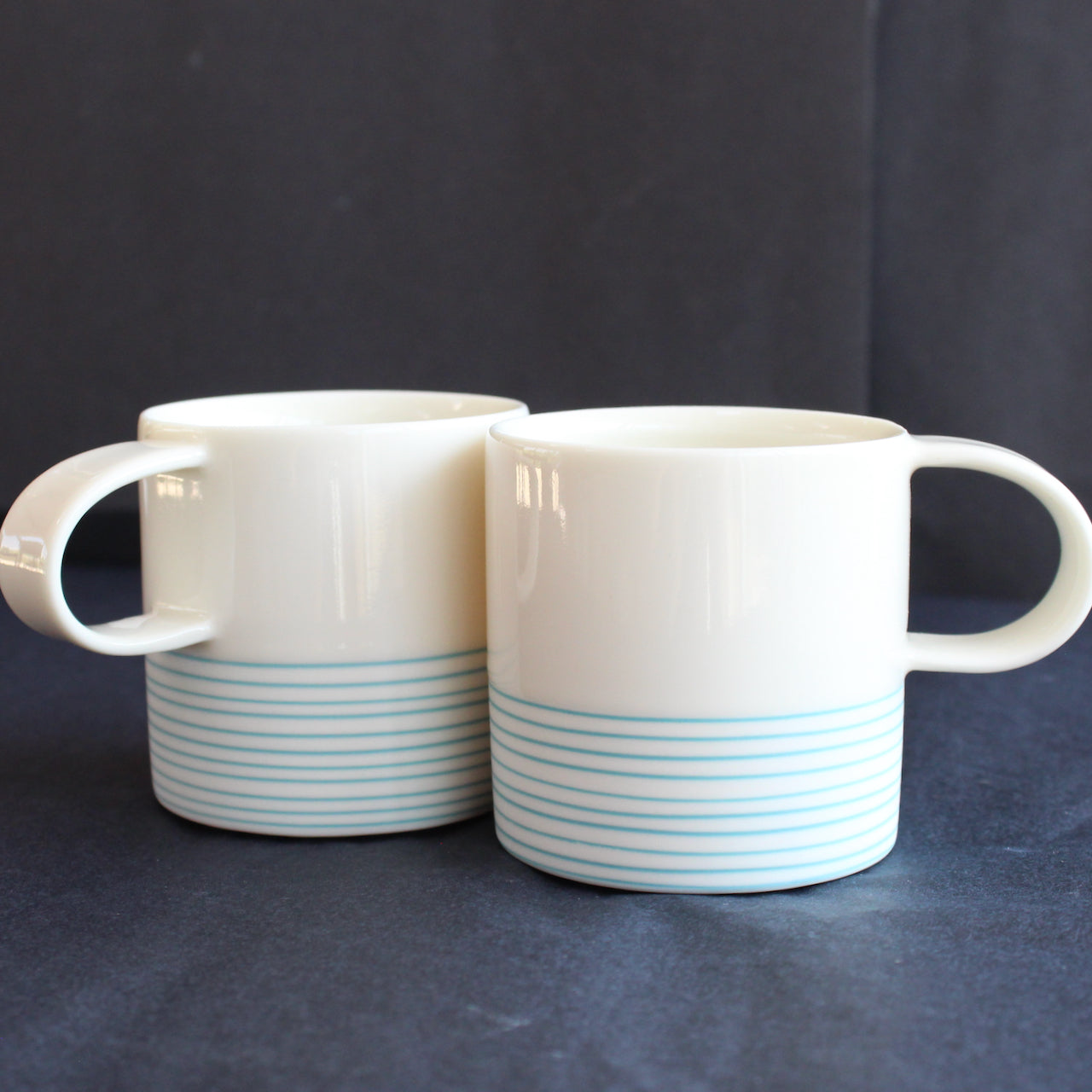 pair of small espresso style cups by Kathryn Sherriff of By the Line Pottery they are in white porcelain with a turquoise ring design around the bottom half