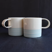 a pair of small espresso style cups by Kathryn Sherriff of By the Line Pottery they are in white porcelain with a turquoise ring design around the bottom half of each cup