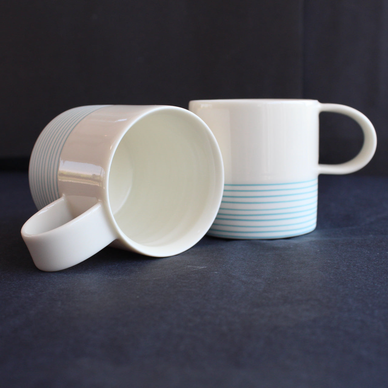 two espresso style cups by Kathryn Sherriff of By the Line Pottery they are in white porcelain with a turquoise ring design around the bottom half 